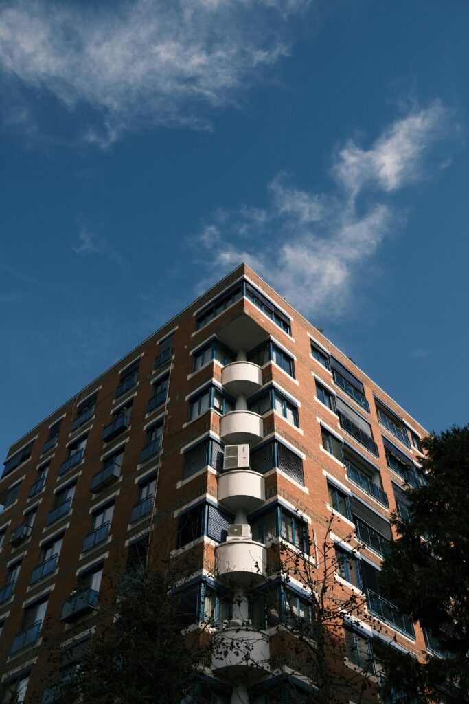 pexels-photo-17872459-17872459 Low angle view of a modern red brick apartment building under a clear blue sky.